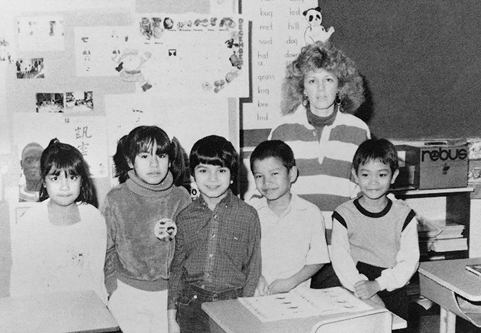 Black and white photograph of an ESL class from our 1987 to 1988 yearbook. Five children and a teacher are pictured. They are standing in a classroom in front of the blackboard.