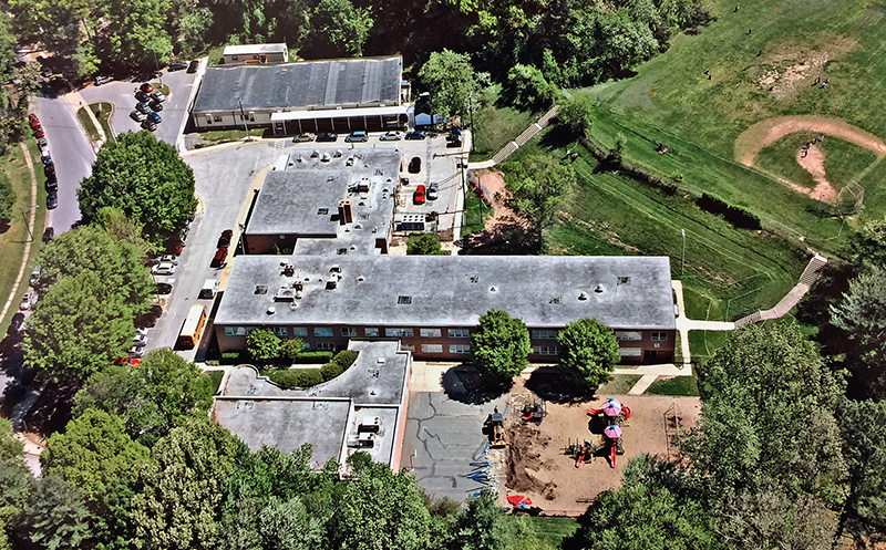 Color aerial photograph of Beech Tree Elementary School. The building is shaped like the letter T. The camera is positioned southwest of the school with the gymnasium and music classroom addition in the foreground, the original two-story classroom wing in the center, and the cafeteria at the top. A modular classroom building can be seen northeast of the main building. 
