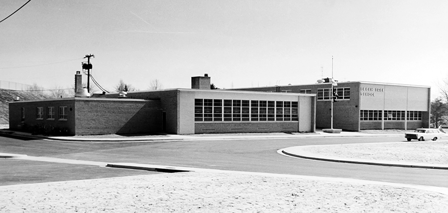 Black and white photograph of the front exterior of Beech Tree Elementary School taken in the late 1960s shortly after the school opened. Pictured are the original cafeteria wing and two story classroom wing. A 1960s era station wagon is parked in front of the school.  