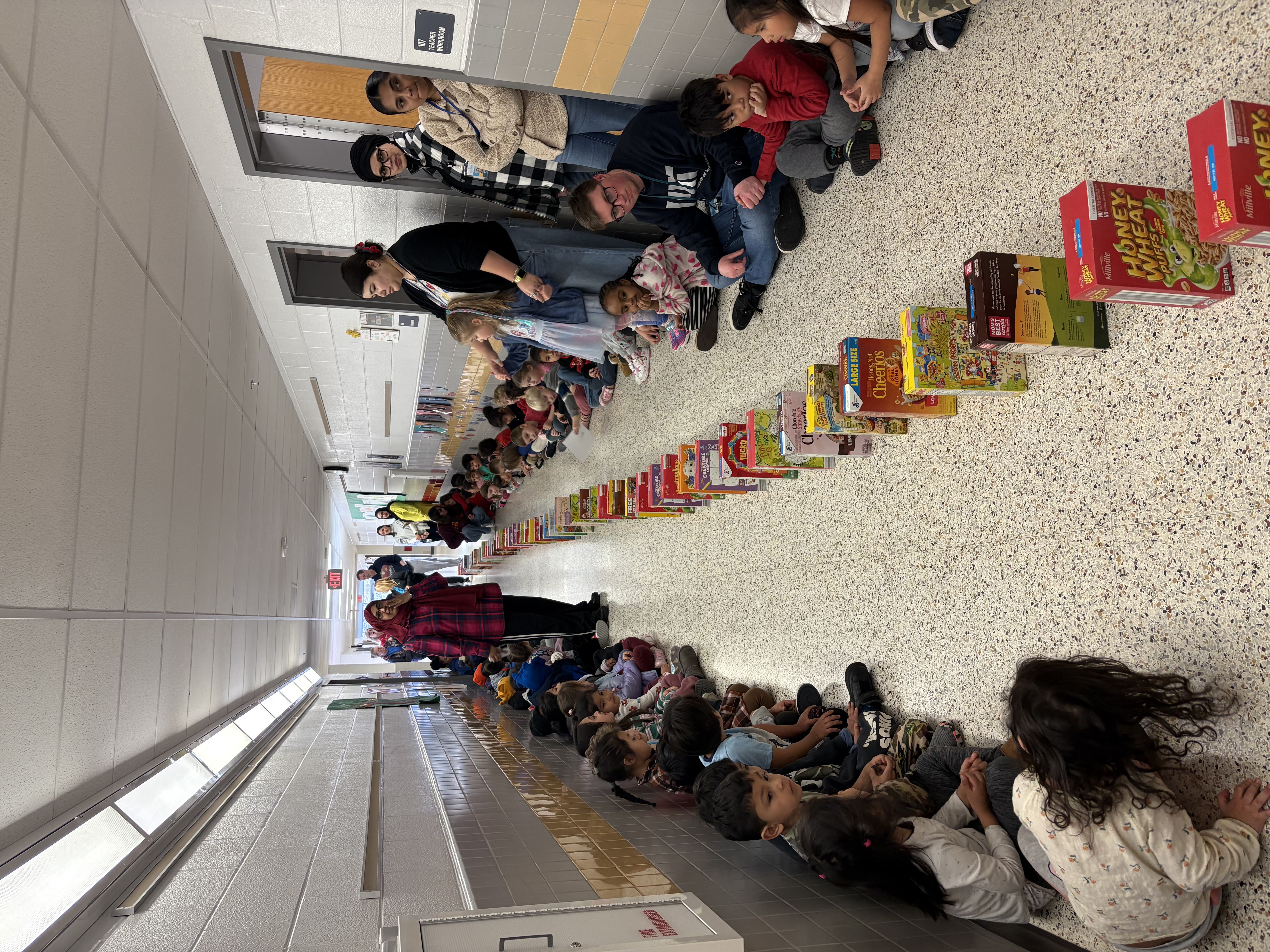 students waiting in the hallway sitting down for the cereal domino event .